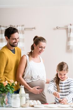 Family with pregnant mother, father and daughter baking together in kitchen