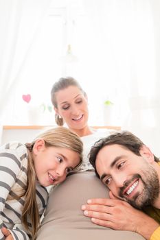 Girl and dad listening at moms belly for soon-to-be sibling