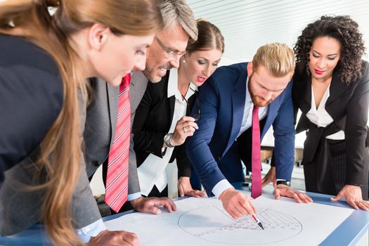 Group of business people are leaning over a desk and analyze graphs