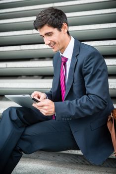 Young businessman smiling while using a tablet PC for online communication or data storage outdoors