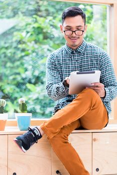 Young Asian man wearing casual clothes while browsing the internet on a tablet PC in the office during break