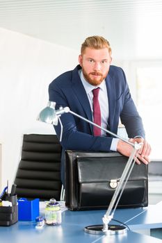 Boss standing at his desk and leaning over his briefcase