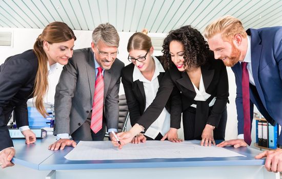 Group of business people are leaning over a desk and analyze graphs