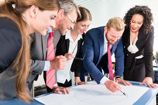 Group of business people are leaning over a desk and analyze graphs