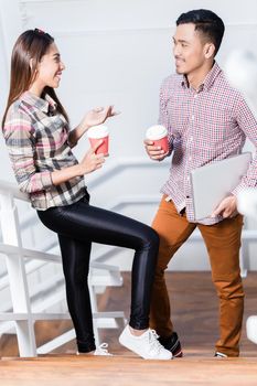 Happy young man and woman talking while drinking coffee from disposable cups during break at work