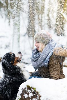 Woman walking her dog in the winter and both explore the snow together in playful mood