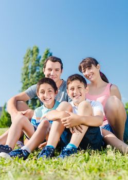 Happy family dressed in white in park in summer sitting in meadow