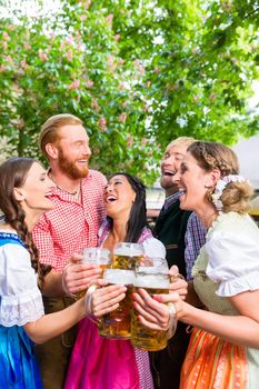 Five friends, men and women, having fun in beer garden clinking glasses with beer