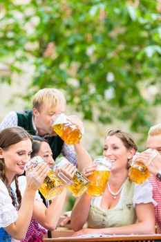 Four friends drinking beer at the same time in Bavarian beer garden