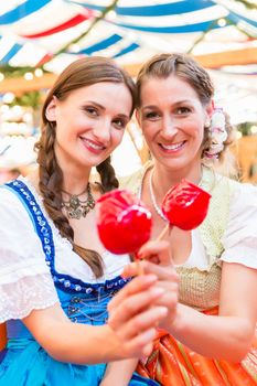 Two friends wearing dirndl and holding candy apples in a beer tent at Regensburger Dult