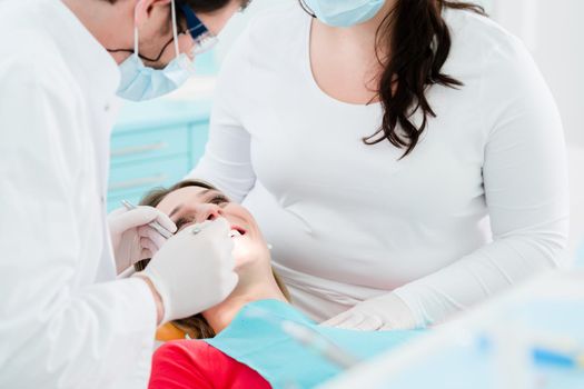 Zahnarzt behandelt Patientin in Praxis zusammen mit Zahnarzthelferin