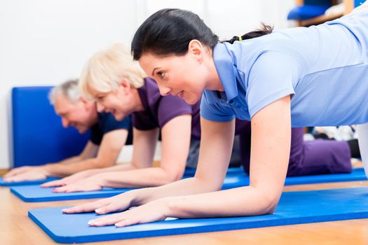 Senior woman and man doing floor gymnastics with physiotherapist