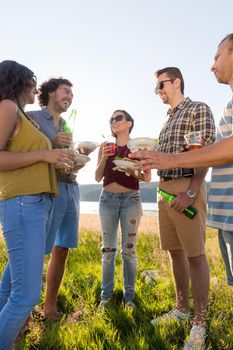 Circle of friends on summer BBQ party at lakeside having burgers and beer