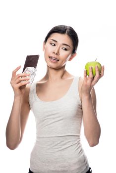 Funny young woman eating a fresh apple while looking at a chocolate bar