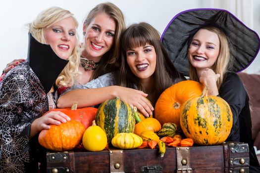 Four cheerful beautiful women toasting while celebrating Halloween together during costume party indoors in a decorated room