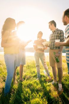 Circle of friends on summer BBQ party at lakeside having burgers and beer