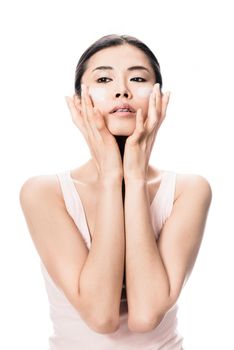 Young woman applying anti-aging soft moisturizer on her cheeks against white background