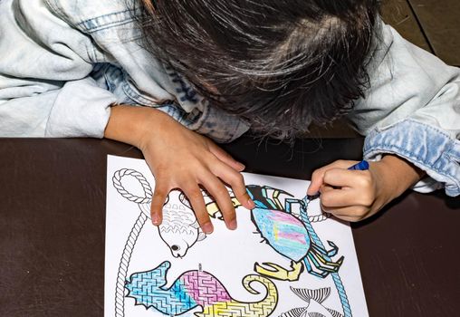 Pretty asian child left handed while doing a coloring activity with crayon and coloring book