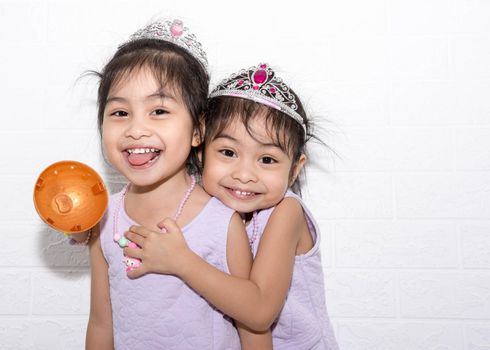 Female asian identical twins sitting on chair with white background. Wearing purple dress and accessories. Hugging each other while standing and smiling