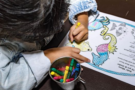 Pretty asian child left handed while doing a coloring activity with crayon and coloring book