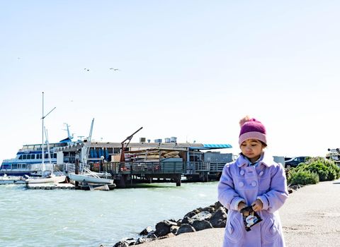 Pretty female child wearing purple coat and cute bonnet while walking and eating snacks from a bay area in Sausalito California