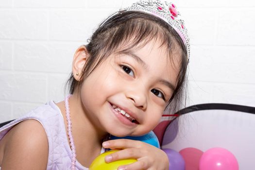 Female asian child girl  while sitting and playing with colorful plastic balls while wearing accessories like crown and necklace