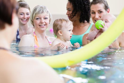 Small kids and their happy mothers playing with balls at baby swimming course