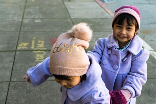 Female child twins wearing purple coat and cute bonnet and gloves while playing