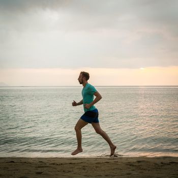 Full length side view of an athletic young man running on the beach during cardio workout session in summer vacation in Indonesia