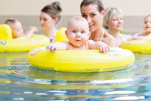 Mums and their children having fun together playing with toys at baby swimming lesson