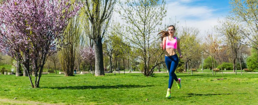 Woman running for better fitness though a park in spring