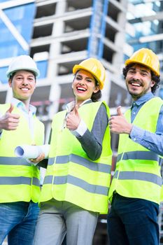 Team of civil engineers and architects at construction site giving thumbs up gesture and saying OK