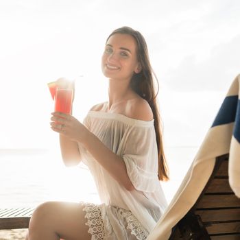 High-key portrait of a beautiful young woman smiling while enjoying a cocktail on a tropical beach during summer vacation in Flores Island, Indonesia
