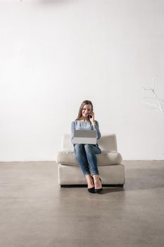 Young woman sitting inwhite room using smartphone and notebook PC