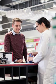 Portrait of a handsome young man and happy customer listening to the recommendations and the advice of a reliable female pharmacist in a contemporary drugstore