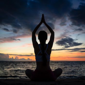 Full length rear view of a fit woman sitting in lotus position while practicing yoga on the beach at twilight during summer vacation in Flores Island, Indonesia