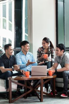 Team of four dedicated employees sitting in front of a laptop while working together at an innovative business project in a modern office