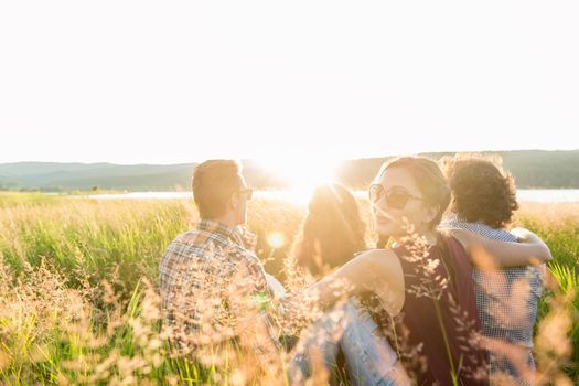 Friends sitting together at lake in summer enjoying sundown and evening mood