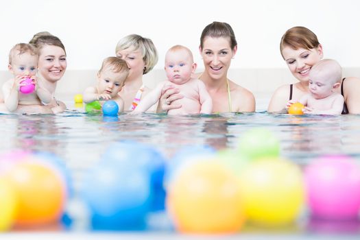 Moms and children at infant swimming lesson playing with balls