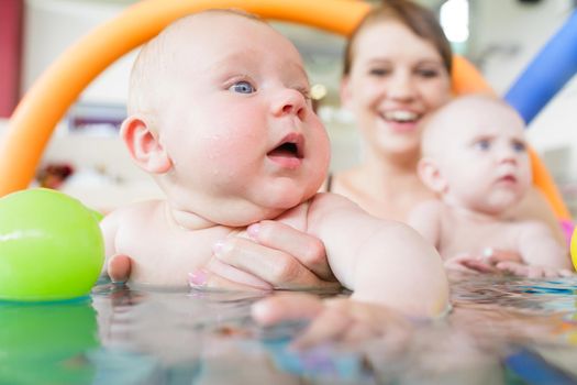 Newborn baby in pool at infant swimming lesson reaching for water ball
