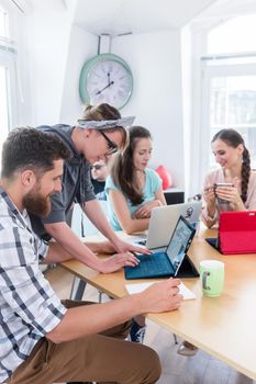 Cheerful young man and woman cooperating for finding solutions while working together online as co-workers in a modern collaborative office space