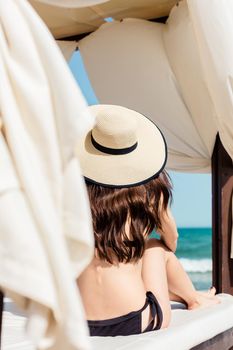 Woman on the beach in sun tent looking at the sea