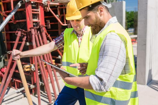 Two young construction workers smiling while using a tablet for online communication through social media during break at work