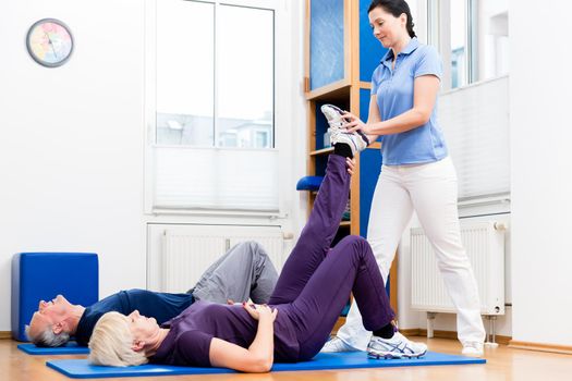 Senior woman and man doing assisted floor exercises with physiotherapist