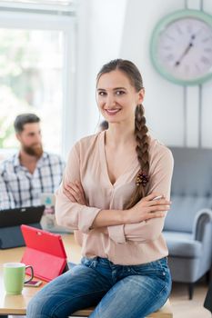 Portrait of a successful entrepreneur looking at camera while sitting on a desk in the shared office space of a work hub for independent contractors