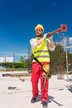 Full length of a blue-collar worker wearing safety equipment, while carrying a heavy metallic bar during work on the construction site of a residential building