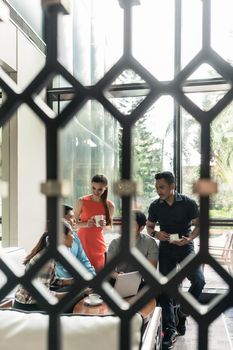 Full length of a multi-ethnic group of five cheerful employees drinking coffee, while watching a funny video on laptop during break in the lounge area of a modern multinational company