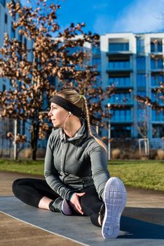 Fit young woman with a healthy lifestyle daydreaming while stretching her leg on a mat during outdoor warm-up exercises in a sunny day