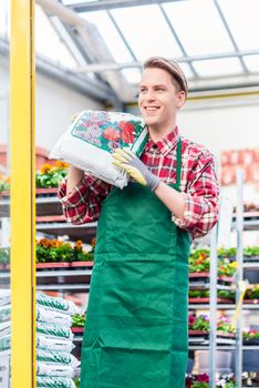 Portrait of a cheerful young man carrying a bag of high-quality potting soil while working as floristry specialist in a modern flower shop