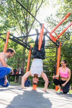 Full length of a determined young man practicing handstand motivated by his positive friends during outdoor workout in a modern calisthenics park